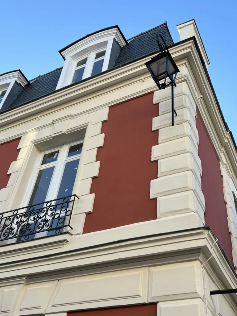 Angle d’une maison bourgeoise à comble mansardé après le ravalement : panneaux rouges, chaînes d’angle et encadrements en relief