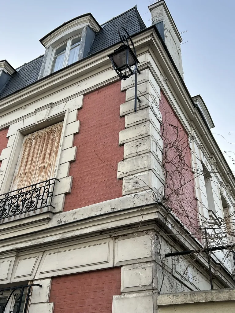 Corner of a townhouse before the facade work: flaking paint on the quoins, rusted shutter, dead ivy