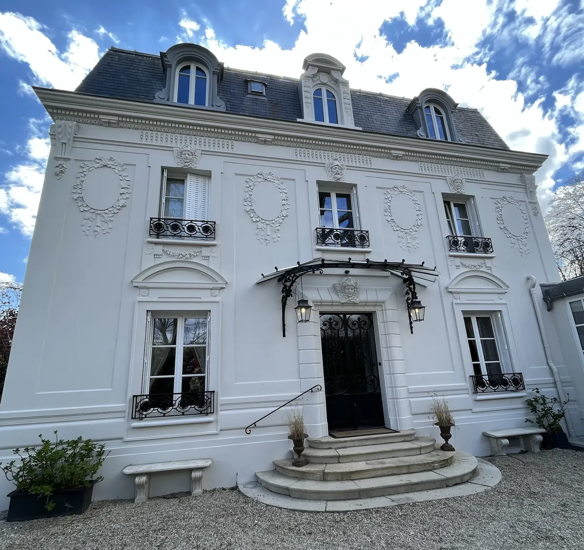 Maison de maître à façade blanche, guirlandes, mascarons et marquise en fer forgé