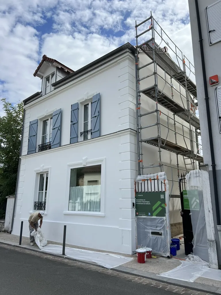 Maison de ville à volets bleus pendant les travaux : façade sur rue refaite, pignon sous échafaudage