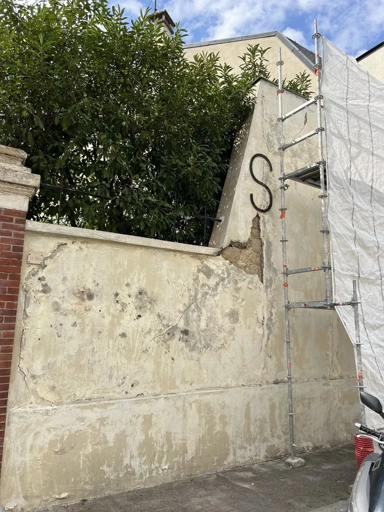 Mur de clôture avant les travaux : enduit fissuré et décollé, maçonnerie à nu, échafaudage en place